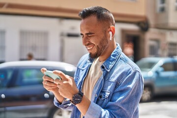 Obraz na płótnie Canvas Young hispanic man smiling confident watching video on smartphone at street