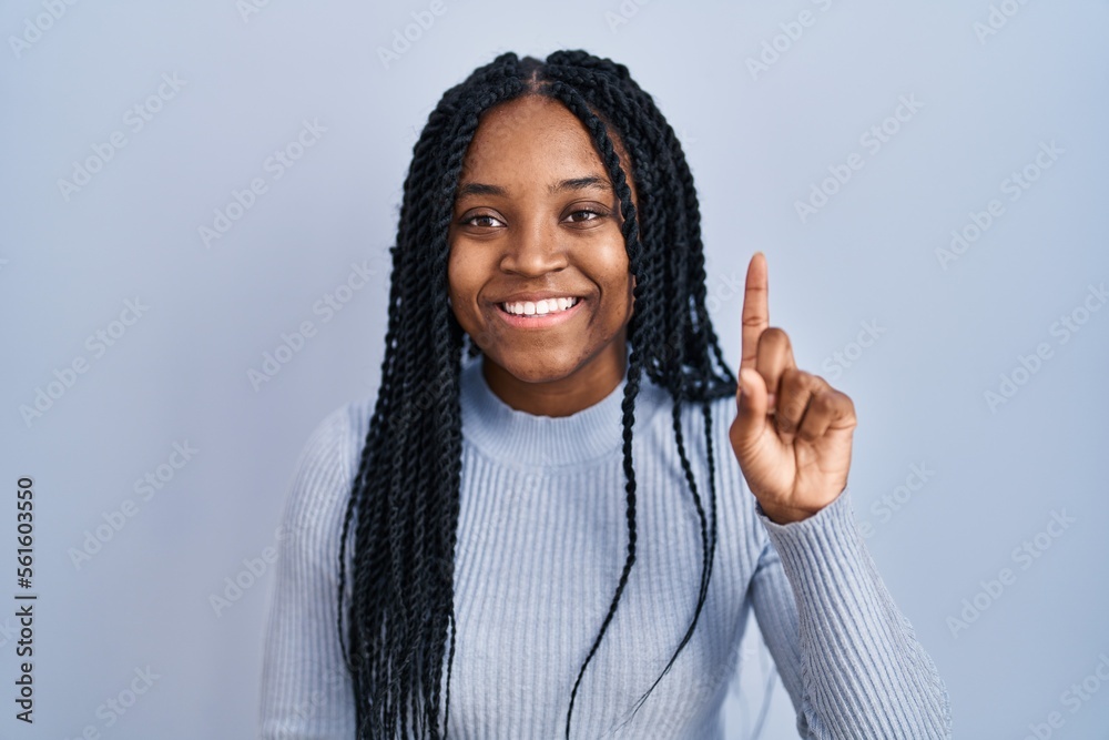 Poster African american woman standing over blue background showing and pointing up with finger number one while smiling confident and happy.