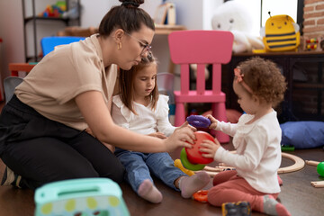 Teacher with girls playing with hoops toys sitting on floor at kindergarten