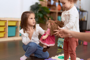 Two little girls playing with dolls sitting on floor at kindergarten