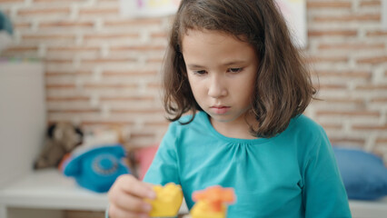 Adorable chinese girl playing with construction blocks sitting on table at kindergarten