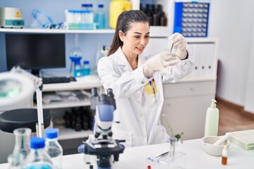 Fototapeta premium Young beautiful hispanic woman scientist smiling confident mixing sample at laboratory