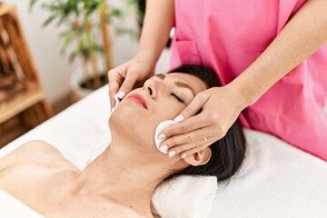 Fototapeta na wymiar Middle age hispanic woman having facial treatment cleaning face at beauty center