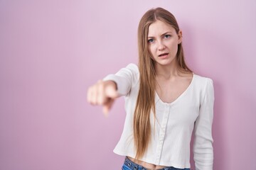 Young caucasian woman standing over pink background pointing displeased and frustrated to the...