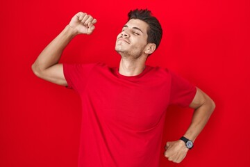 Young hispanic man standing over red background stretching back, tired and relaxed, sleepy and yawning for early morning