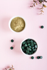 Obraz na płótnie Canvas Detox and antioxidant. Matcha powder and spirulina pills in bowls on a pink. Top and vertical view