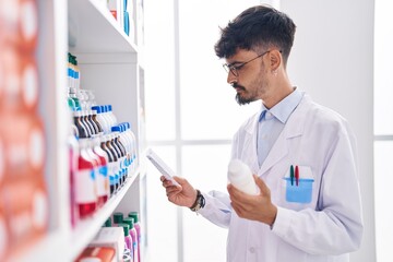 Young hispanic man pharmacist holding pills bottle reading preascription at pharmacy