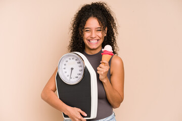 Young african american woman holding a scale and an ice cream isolated