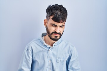 Young hispanic man with beard standing over blue background with hand on stomach because indigestion, painful illness feeling unwell. ache concept.
