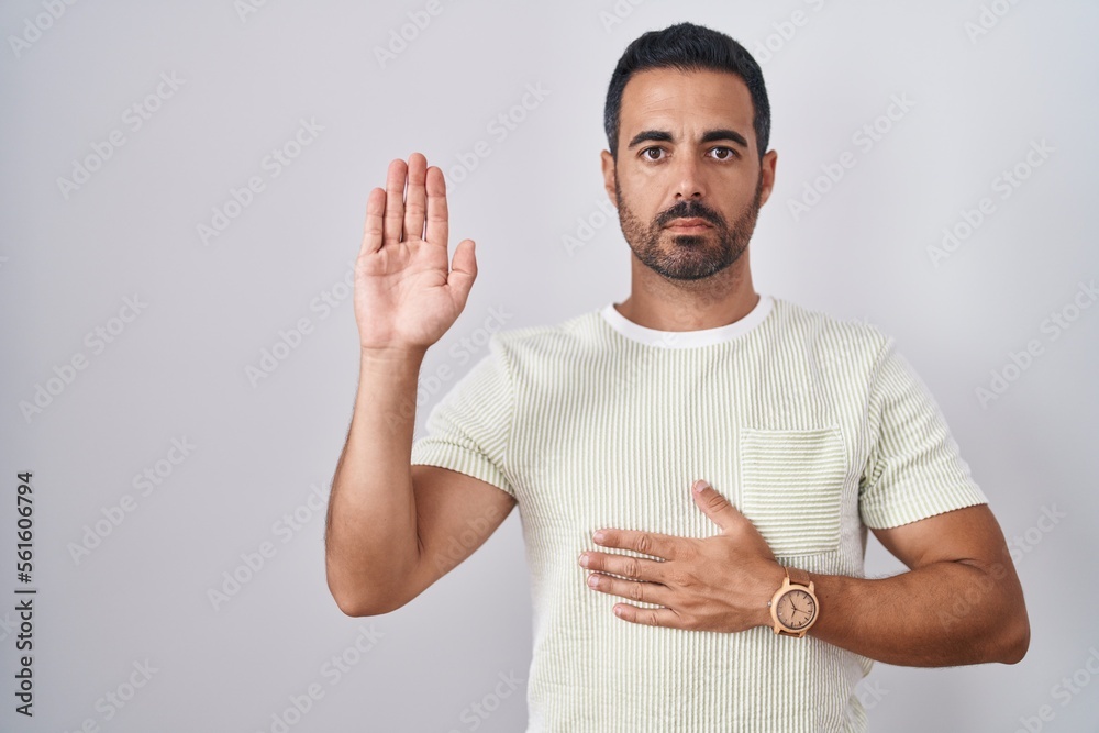 Sticker Hispanic man with beard standing over isolated background swearing with hand on chest and open palm, making a loyalty promise oath