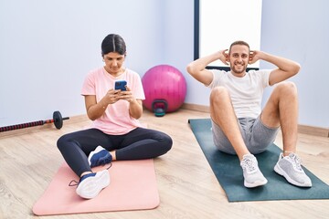 Obraz premium Man and woman couple smiling confident training abs exercise using smartphone at sport center