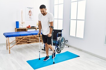 Fototapeta premium Young hispanic man patient having rehab session walking using crutches at clinic
