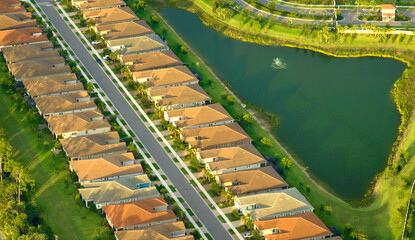 Aerial view of tightly packed homes in Florida closed living clubs with lake water in the middle. Family houses as example of real estate development in american suburbs