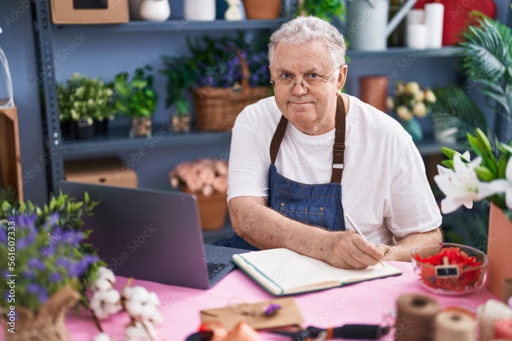 Canvas Prints Middle age grey-haired man florist writing on notebook using laptop at florist