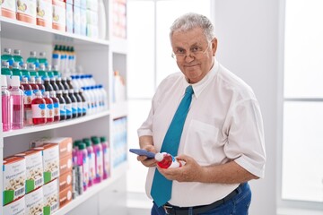 Middle age grey-haired man customer using smartphone holding medicine bottle at pharmacy