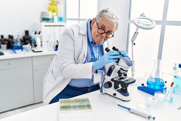 Naklejka premium Middle age grey-haired man wearing scientist uniform using microscope at laboratory