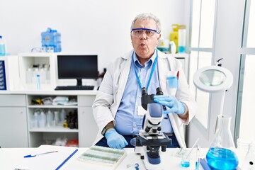 Senior caucasian man working at scientist laboratory making fish face with lips, crazy and comical gesture. funny expression.