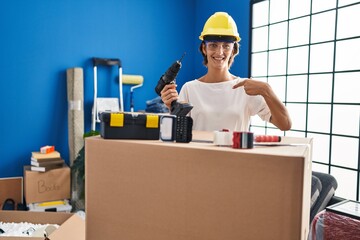 Brunette woman holding screwdriver at new home pointing finger to one self smiling happy and proud