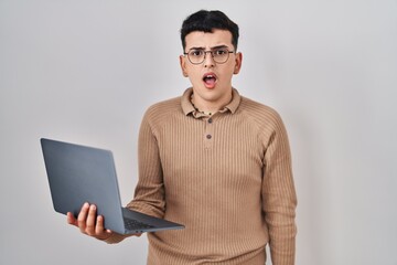 Non binary person using computer laptop in shock face, looking skeptical and sarcastic, surprised with open mouth