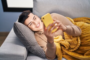 Young non binary man using smartphone lying on sofa at home