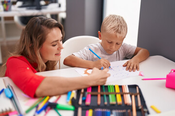 Teacher and toddler sitting on table drawing on paper at classroom