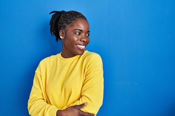 Beautiful black woman standing over blue background looking away to side with smile on face, natural expression. laughing confident. - Powered by Adobe