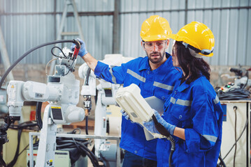 Specialist male and female robotic engineers maintenance and control welding robot arm in factory warehouse, Testing new innovation automation robot for industrial.