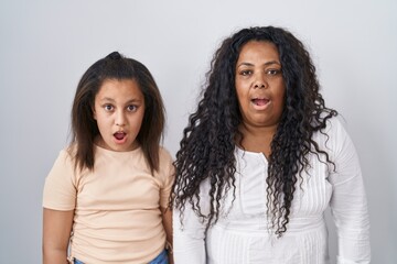 Mother and young daughter standing over white background afraid and shocked with surprise and amazed expression, fear and excited face.