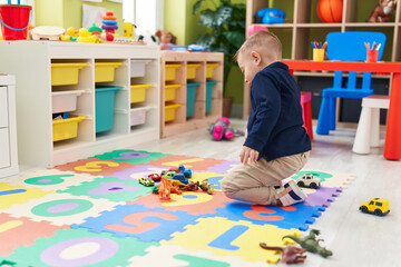 Adorable hispanic boy playing with cars toy sitting on floor at kindergarten
