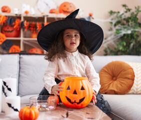 Adorable hispanic girl wearing halloween costume holding pumpkin basket at home