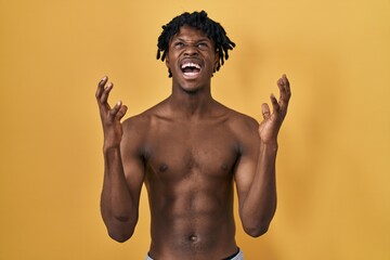 Young african man with dreadlocks standing shirtless crazy and mad shouting and yelling with aggressive expression and arms raised. frustration concept.