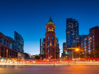 Fototapeta na wymiar Canada, Toronto. The famous Gooderham building and the skyscrapers in the background. View of the city in the evening. Blurring traffic lights. Modern and ancient architecture. Night city.
