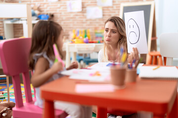 Teacher and toddler sitting on table having emotion therapy at kindergarten