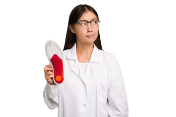 Young asian chiropodist holding a insoles for shoes isolated confused, feels doubtful and unsure.