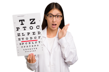 Young asian oculist woman holding a eye chart paper isolated surprised and shocked.