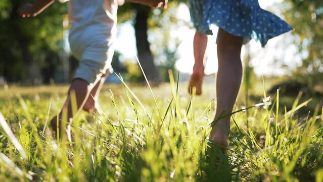 Happy family.Toddlers run barefoot on the green grass in park at sunset.Active running in nature.Summer picnic healthy lifestyle.Legs of children in park on grass.Brother and sister outdoors in summer
