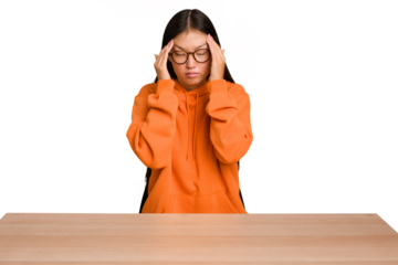 Young asian woman sitting on a table isolated touching temples and having headache.