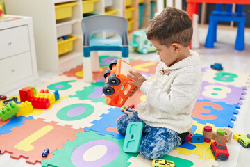 Adorable hispanic toddler playing with cars toy sitting on floor at kindergarten