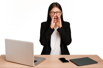 Young business asian woman sitting on a table isolated shouting excited to front.