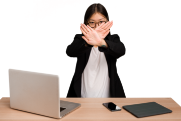 Young business asian woman sitting on a table isolated doing a denial gesture