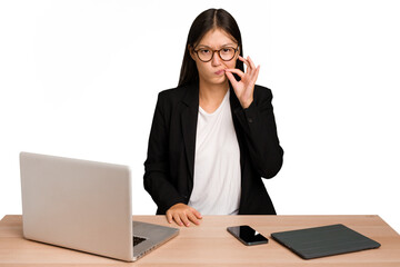 Young business asian woman sitting on a table isolated with fingers on lips keeping a secret.