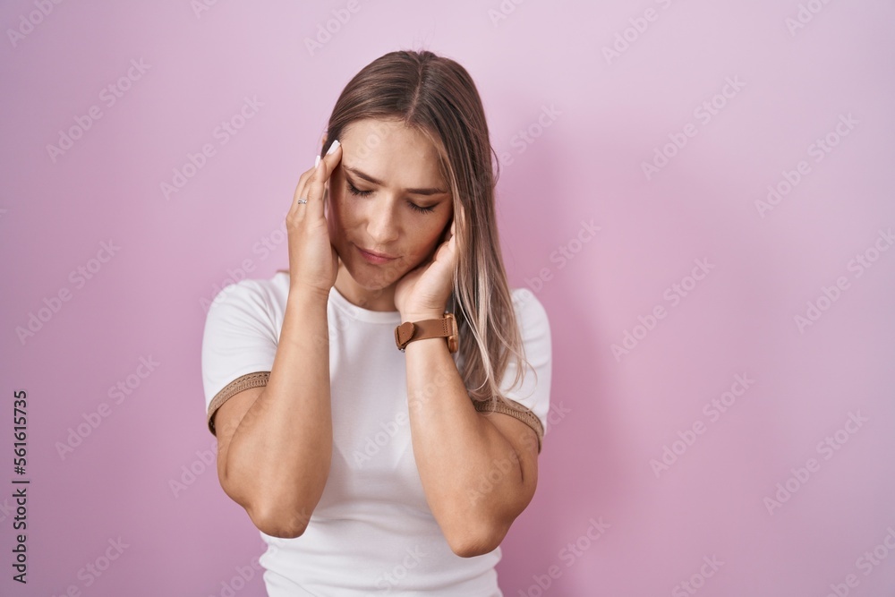 Poster blonde caucasian woman standing over pink background with hand on head, headache because stress. suf