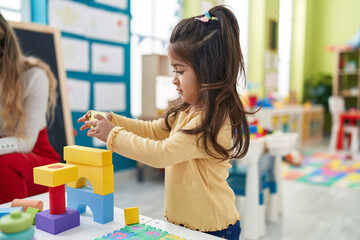 Adorable hispanic girl playing with construction blocks standing at kindergarten