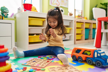 Adorable hispanic girl playing with maths puzzle game sitting on floor at kindergarten