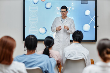 Portrait of young medical professional giving lecture or presentation standing by screen at seminar...