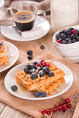 Waffles with red currant and blueberries on white dish.