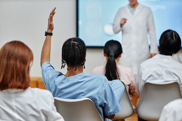 Back view at young black doctor raising hand in audience at medical seminar, copy space