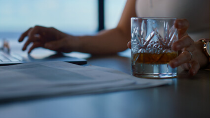 Woman hands typing computer in office closeup. Unknown lady taking whiskey glass
