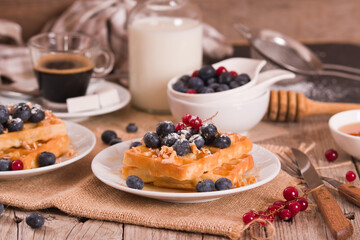 Waffles with red currant and blueberries on white dish.