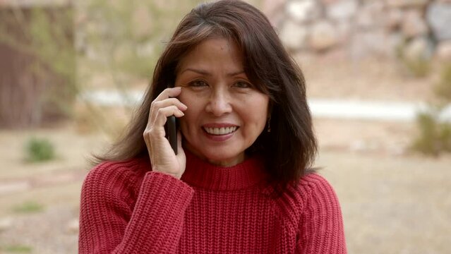 Attractive woman with dimples on smartphone smiles at camera, wind blowing